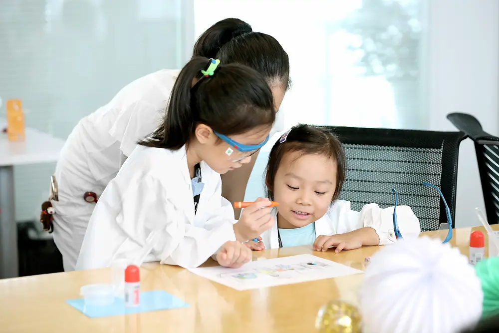 两个孩子和一位女士穿着研究服，在桌子旁画画