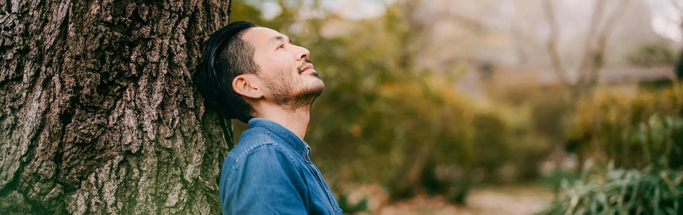 一位男士拿着一本书靠坐在树旁